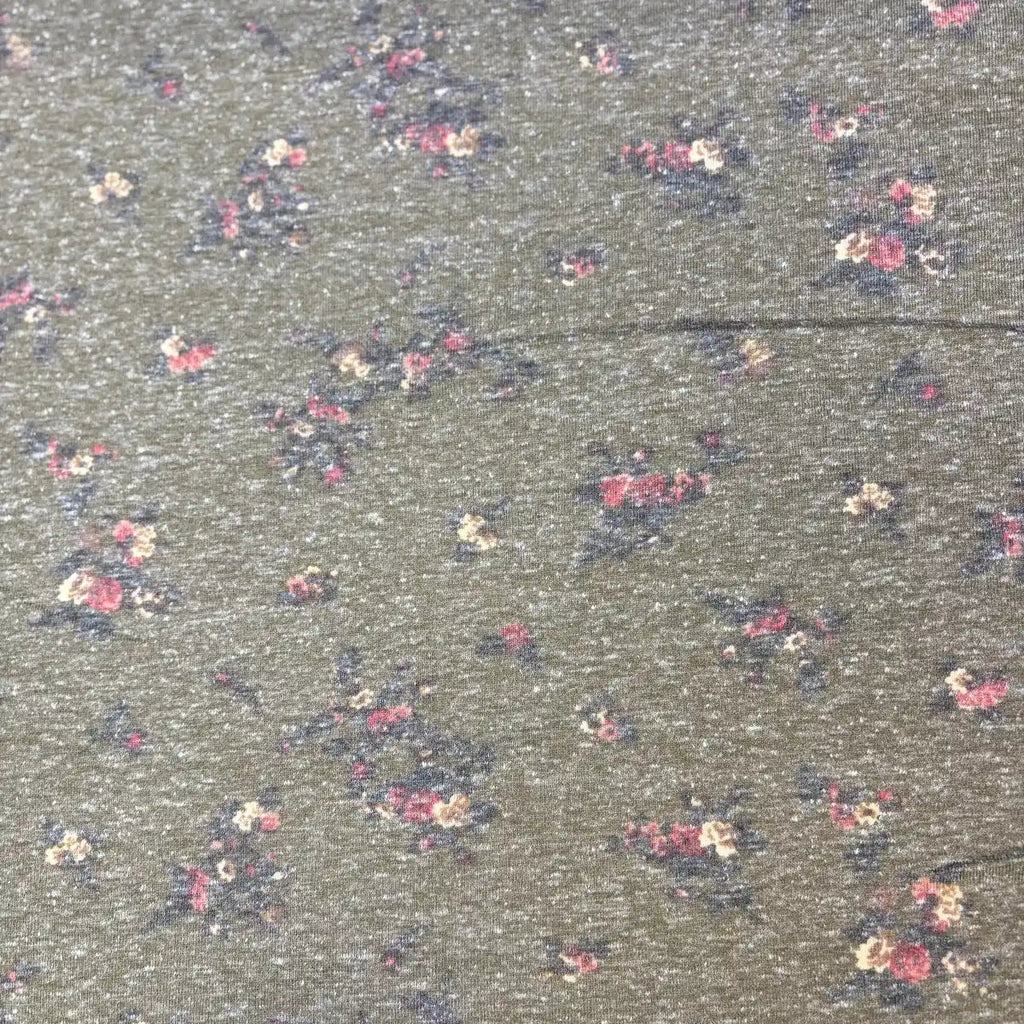 A close-up of a fabric surface with a dense small floral print on a muted gray-green background. The flowers appear in pink, cream, and dark navy tones, repeated across the material.