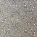 A close-up of a fabric surface with a dense small floral print on a muted gray-green background. The flowers appear in pink, cream, and dark navy tones, repeated across the material.